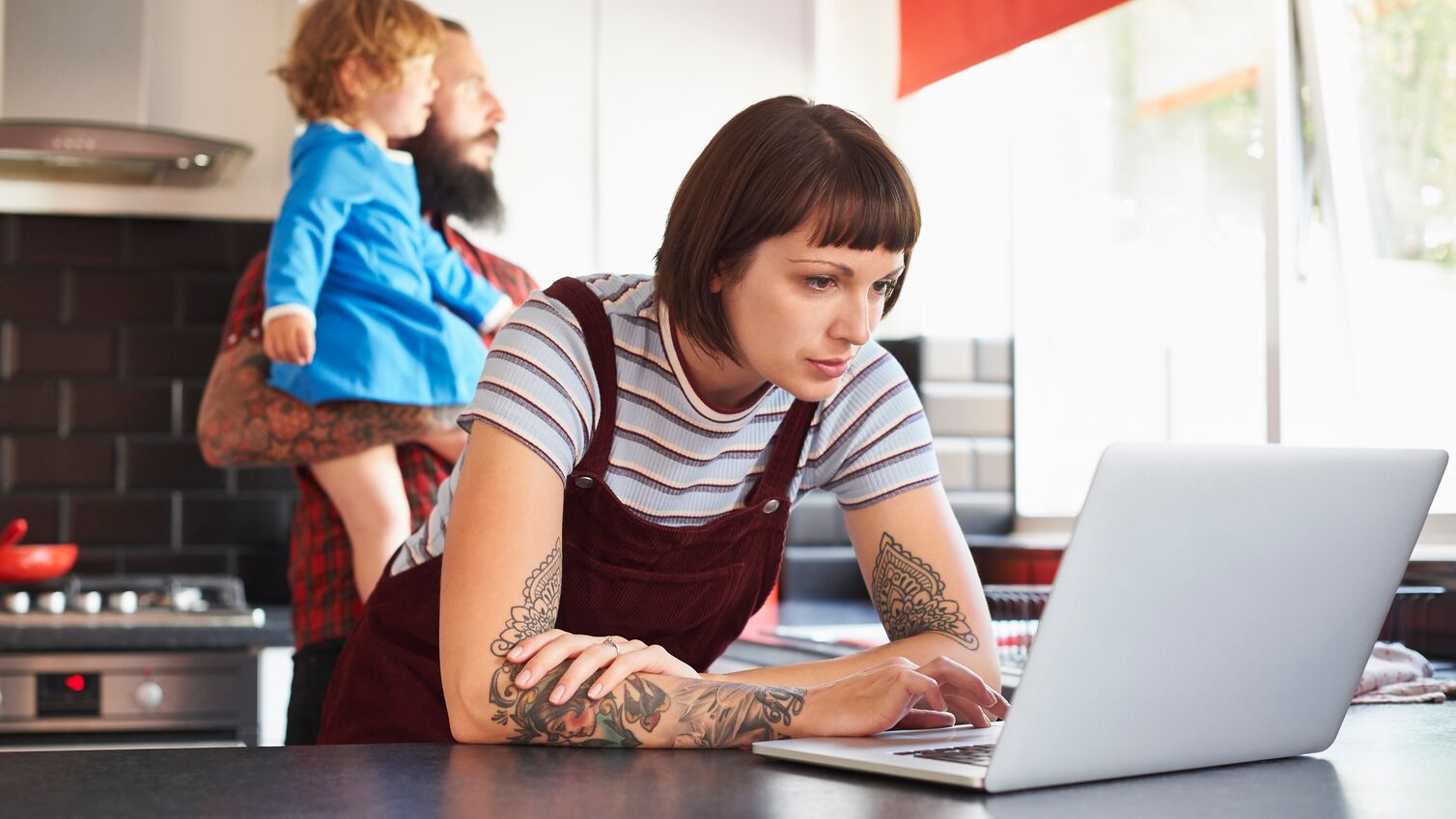 Mum using laptop while Dad looks after their young daughter