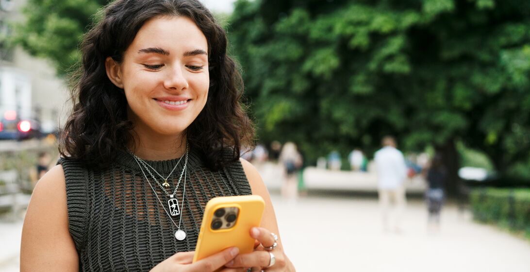 Woman wearing a knitted short sleeved top using her phone with a bright yellow case