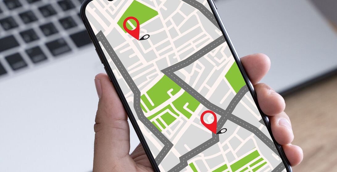 Smartphone device showing GPS map of directions between two locations with a laptop in the background.