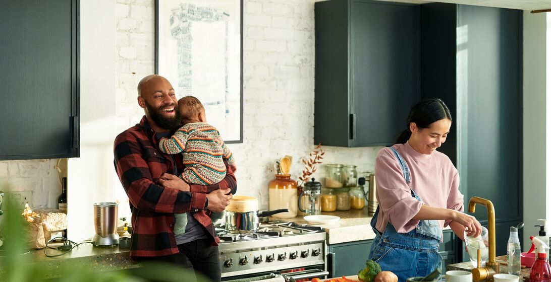 Black father holding baby son, mature Chinese mother at sink, teamwork, cooperation, parenting