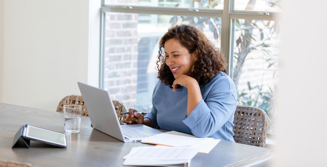 The small business owner smiles while attending a virtual meeting with her financial advisor to review upcoming changes to her taxes.