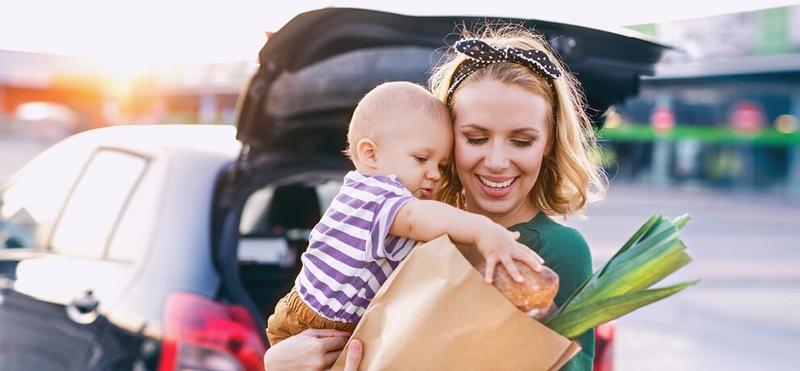 A mum with her baby loading her groceries into her car.