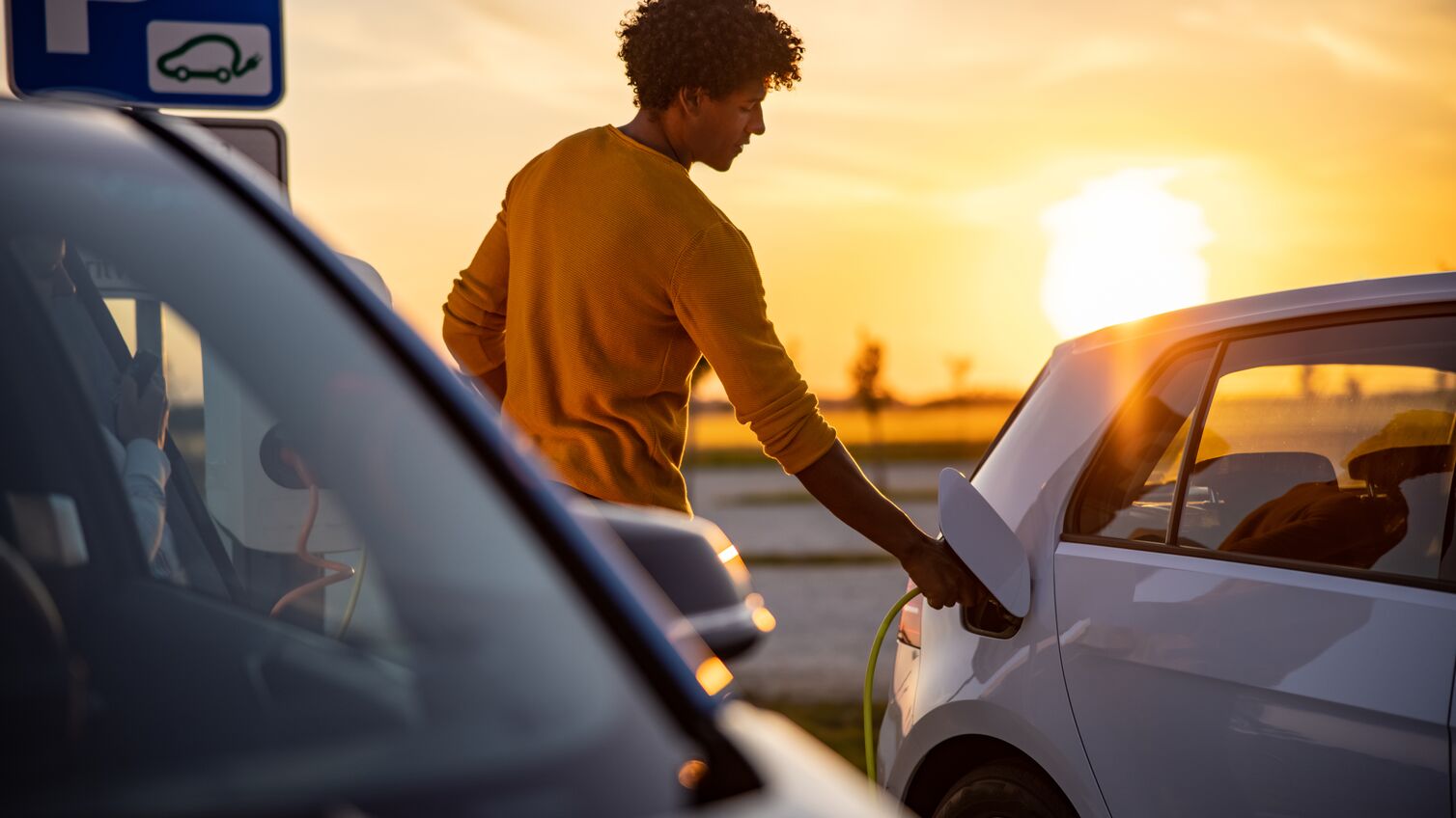 African american man plugging an EV plug into his car for charging at station