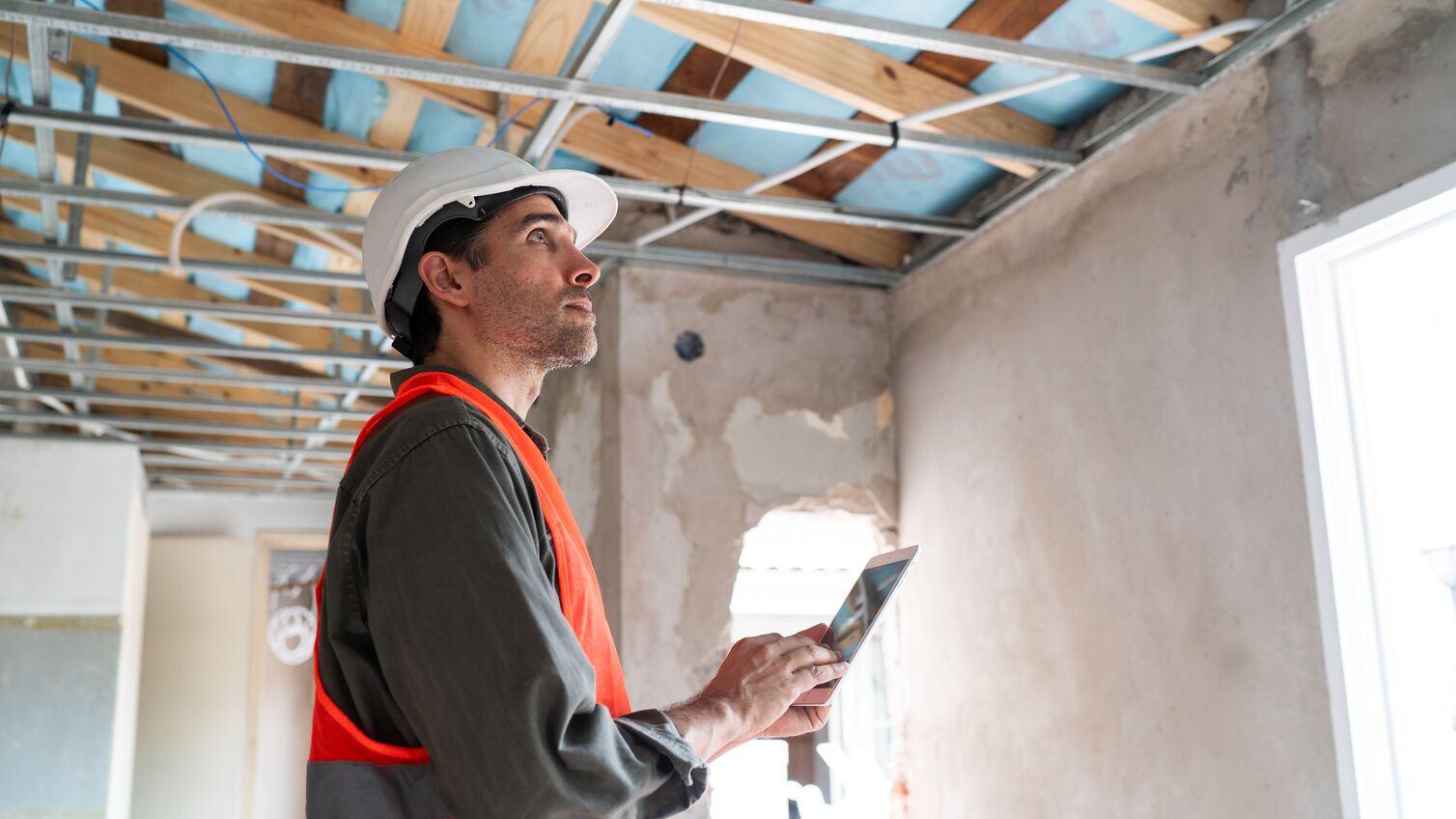 A focused construction supervisor inspects work at a building site, using a digital tablet to check plans and progress.