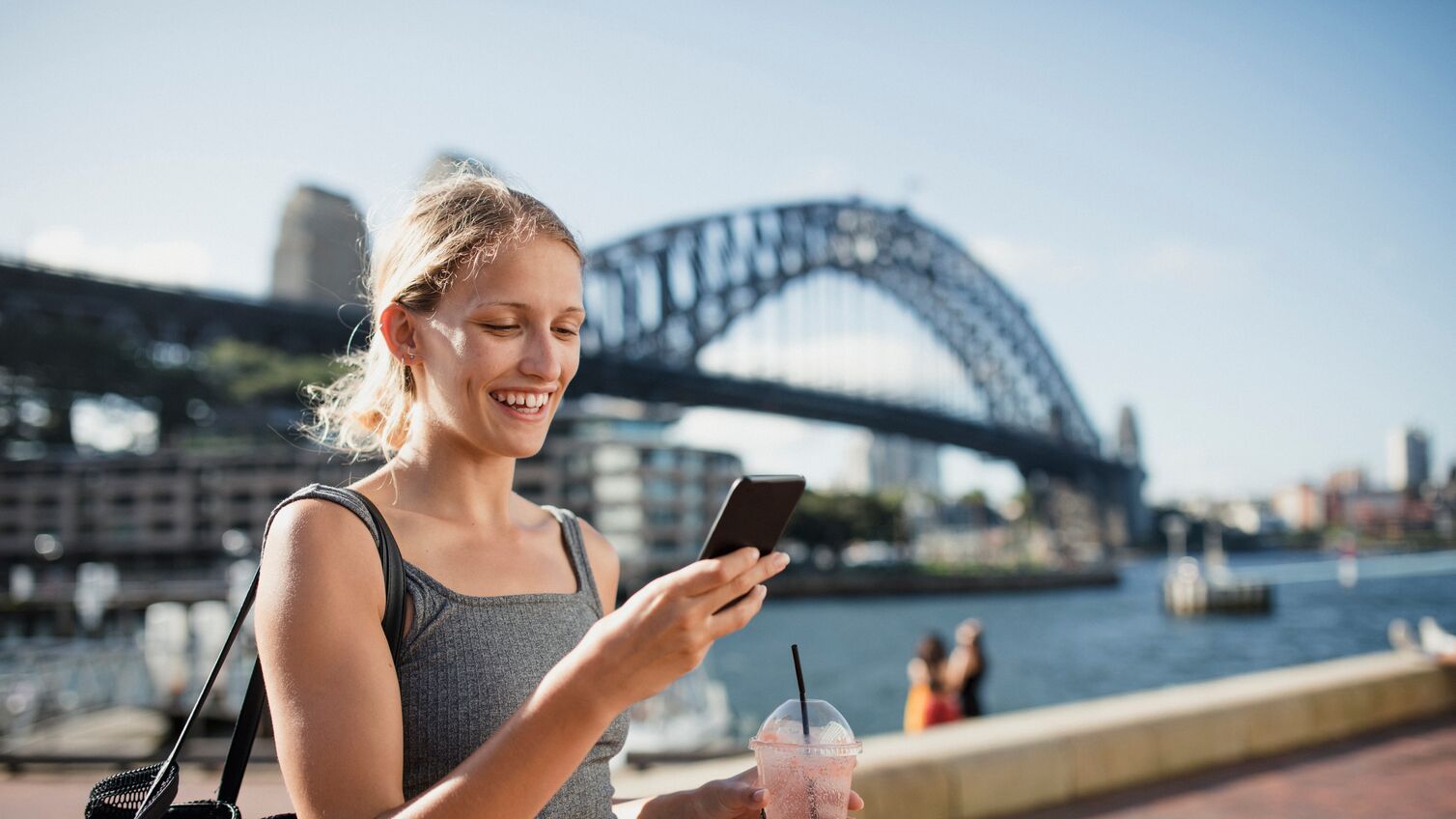 A woman uses her phone with a view of Sydney Harbour Bridge in the background.