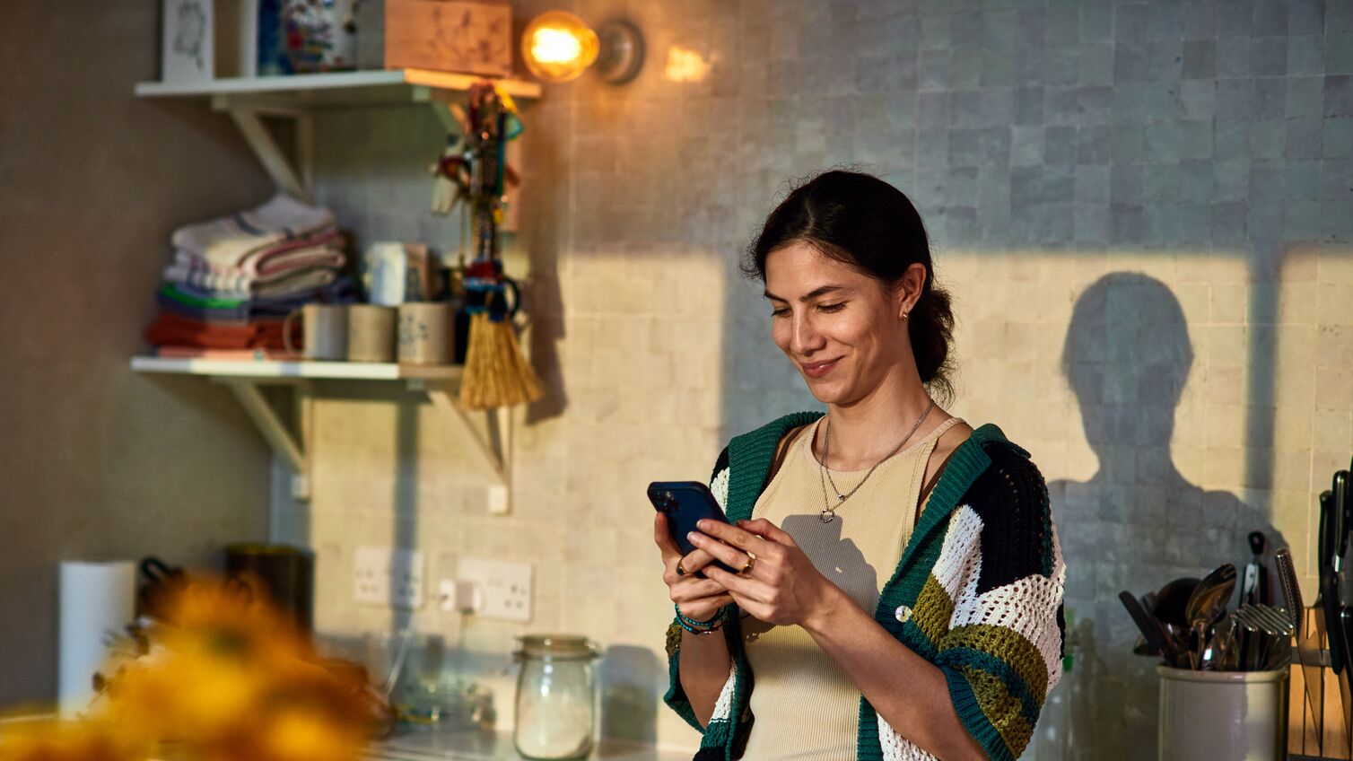 Smiling woman in her 30's standing in kitchen texting on smart phone, communication, wireless technology, the internet