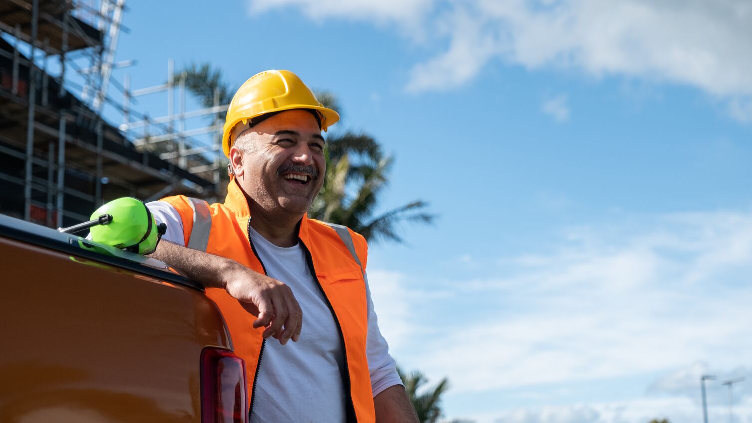 A happy constuction work leaning against the back of a car