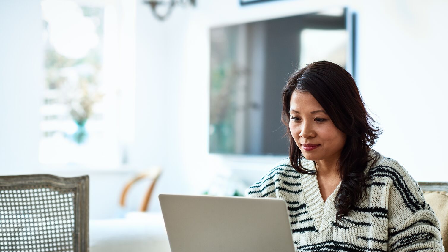 Mid adult woman in her 30s sitting at table and looking at computer, remote working, freelancer, small business