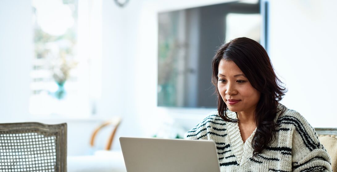 Mid adult woman in her 30s sitting at table and looking at computer, remote working, freelancer, small business