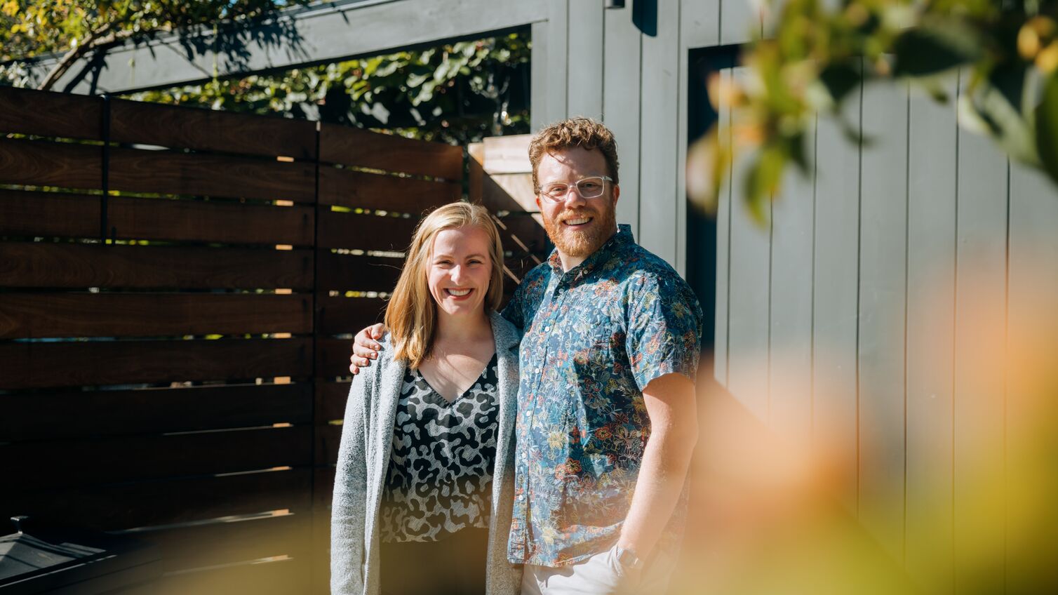 A mid-adult Caucasian man and woman stand outside of their new home, or a home they are representing for sale as realtors. They look at the camera. Shot in Seattle, Washington, USA.