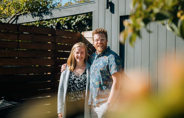 A mid-adult Caucasian man and woman stand outside of their new home, or a home they are representing for sale as realtors. They look at the camera. Shot in Seattle, Washington, USA.