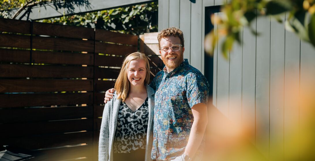 A mid-adult Caucasian man and woman stand outside of their new home, or a home they are representing for sale as realtors.  They look at the camera.  Shot in Seattle, Washington, USA.
