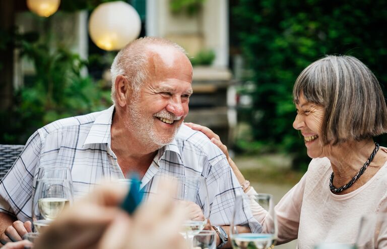 An elderly couople smiling and drinking at a family barbecue in a courtyard.