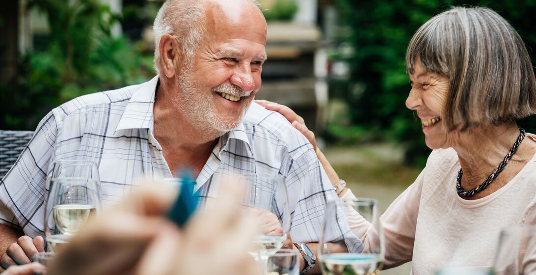 An elderly couople smiling and drinking at a family barbecue in a courtyard.