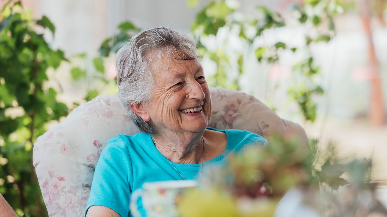 A shot of a senior, Caucasian woman smiling and enjoying a cup of tea outside.