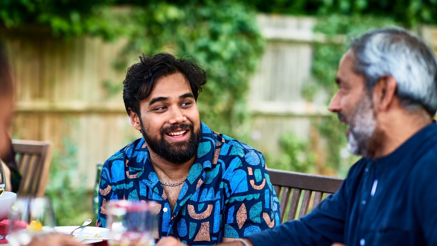 Two men chatting outdoors enjoying food and drink, father and son, adult offspring, family party