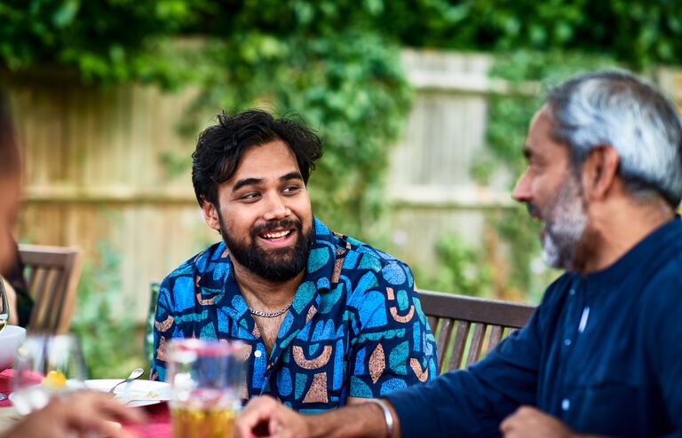 Two men chatting outdoors enjoying food and drink, father and son, adult offspring, family party