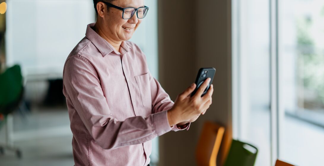 An Asian Chinese businessman using smartphone in office. Text messaging, e-mail, online shopping, ordering, making a reservation, online banking.
