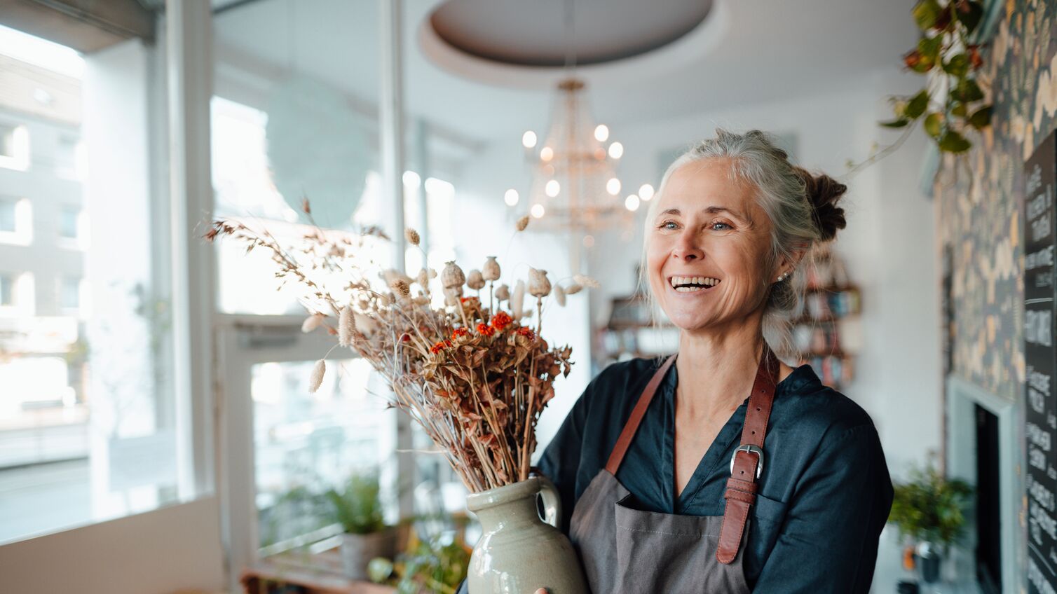 Smiling female cafe owner holding flower vase in coffee shop
