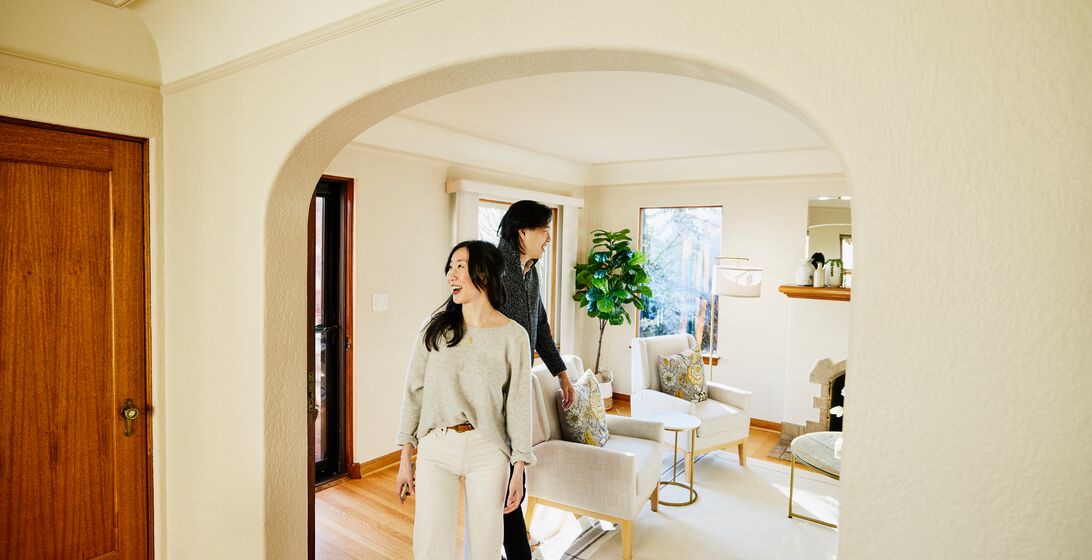 Wide shot of smiling couple walking into home for sale during open house