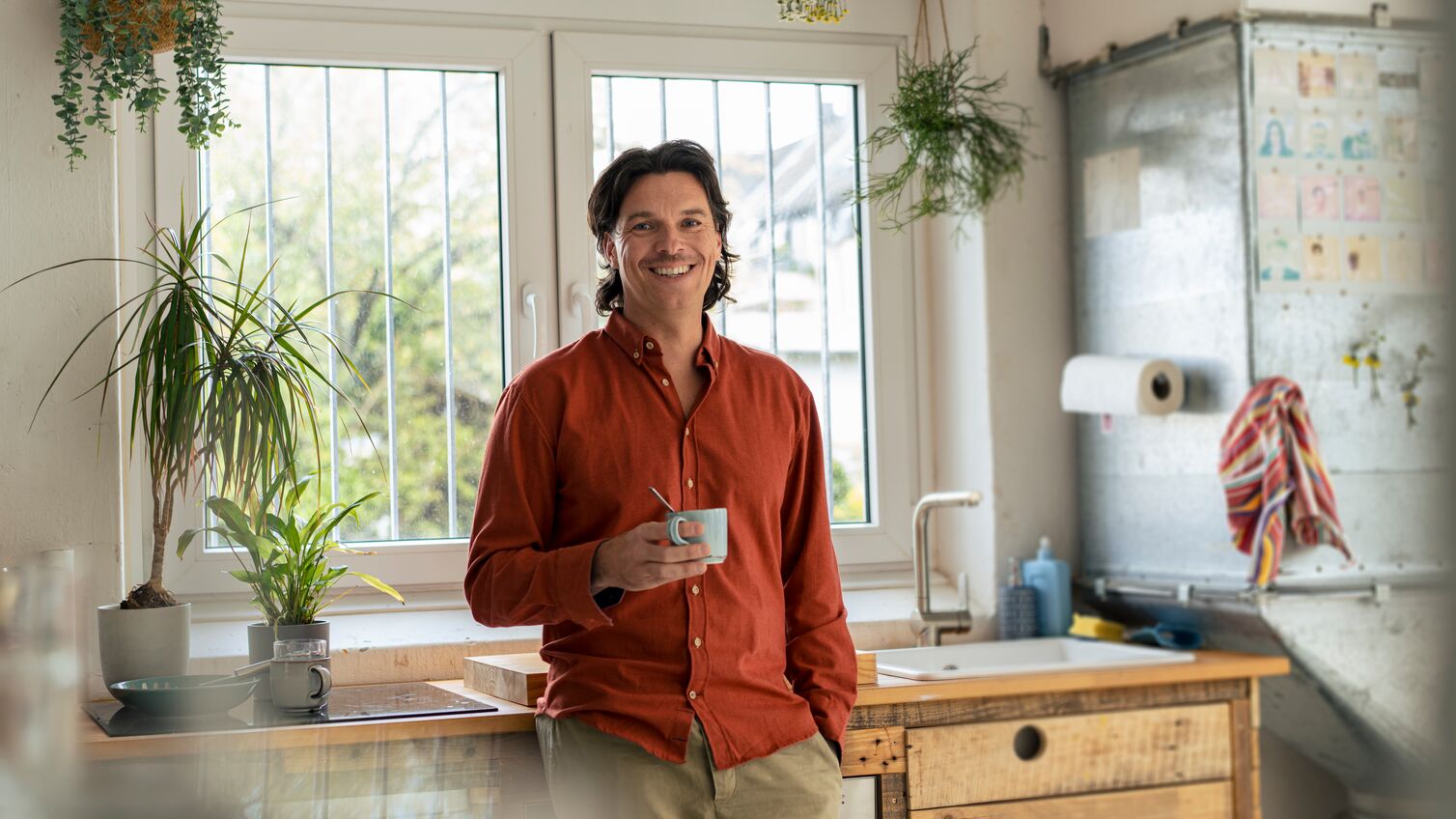 Smiling businessman holding coffee cup and standing in kitchen at home