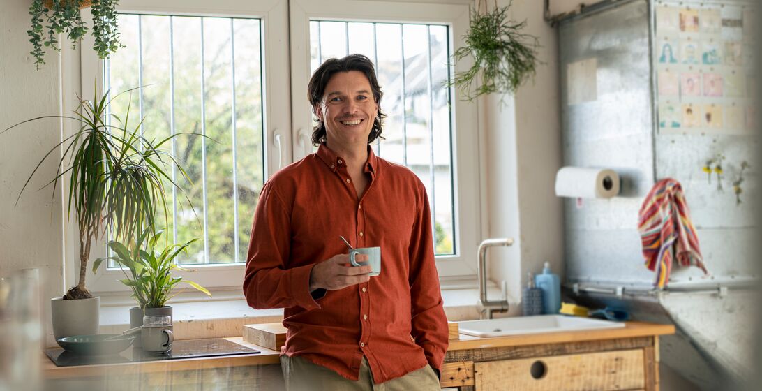 Smiling businessman holding coffee cup and standing in kitchen at home