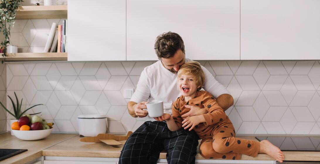 Cheerful father with his little son in kitchen in morning, bonding and looking at camera.