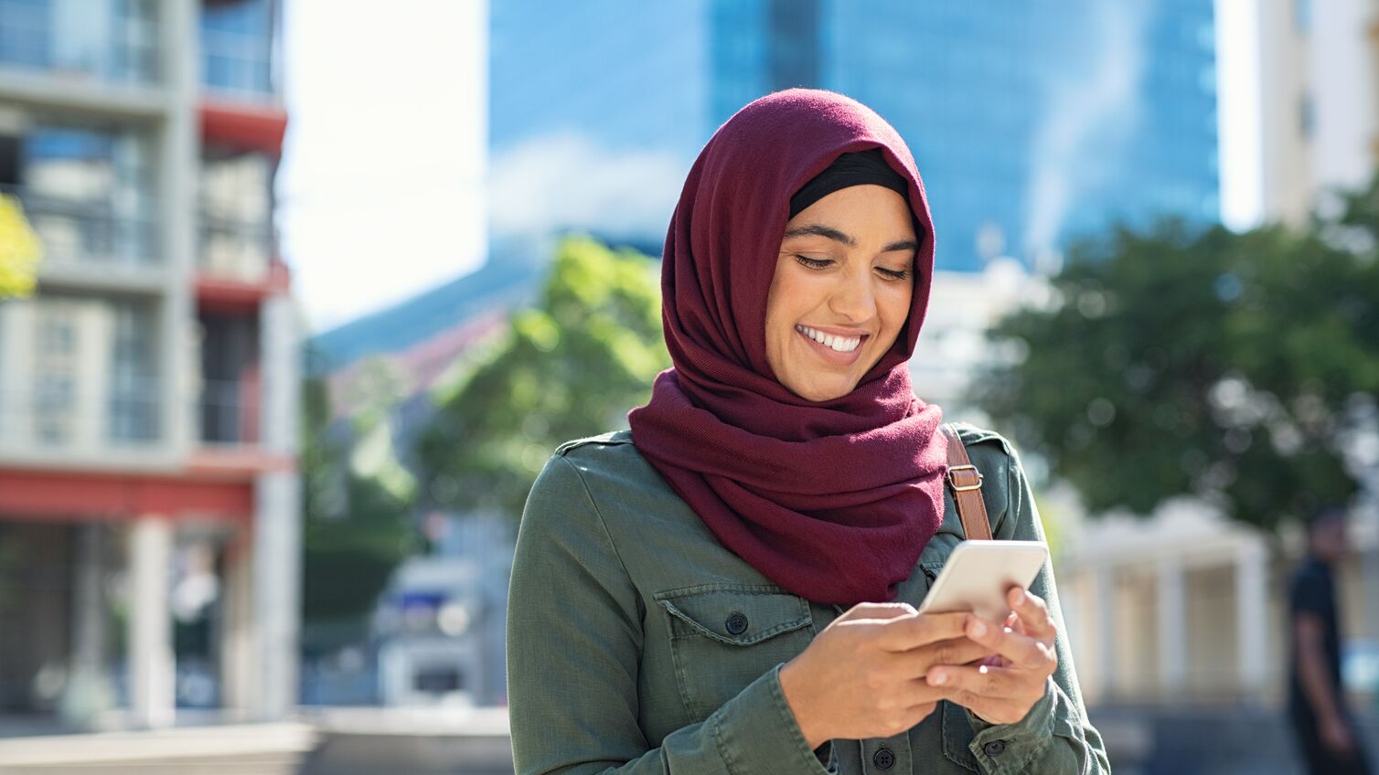 Pretty muslim woman using mobile phone outdoor. Arabic woman wearing hijab using smartphone on the street. Islamic girl texting a message phone in city centre.