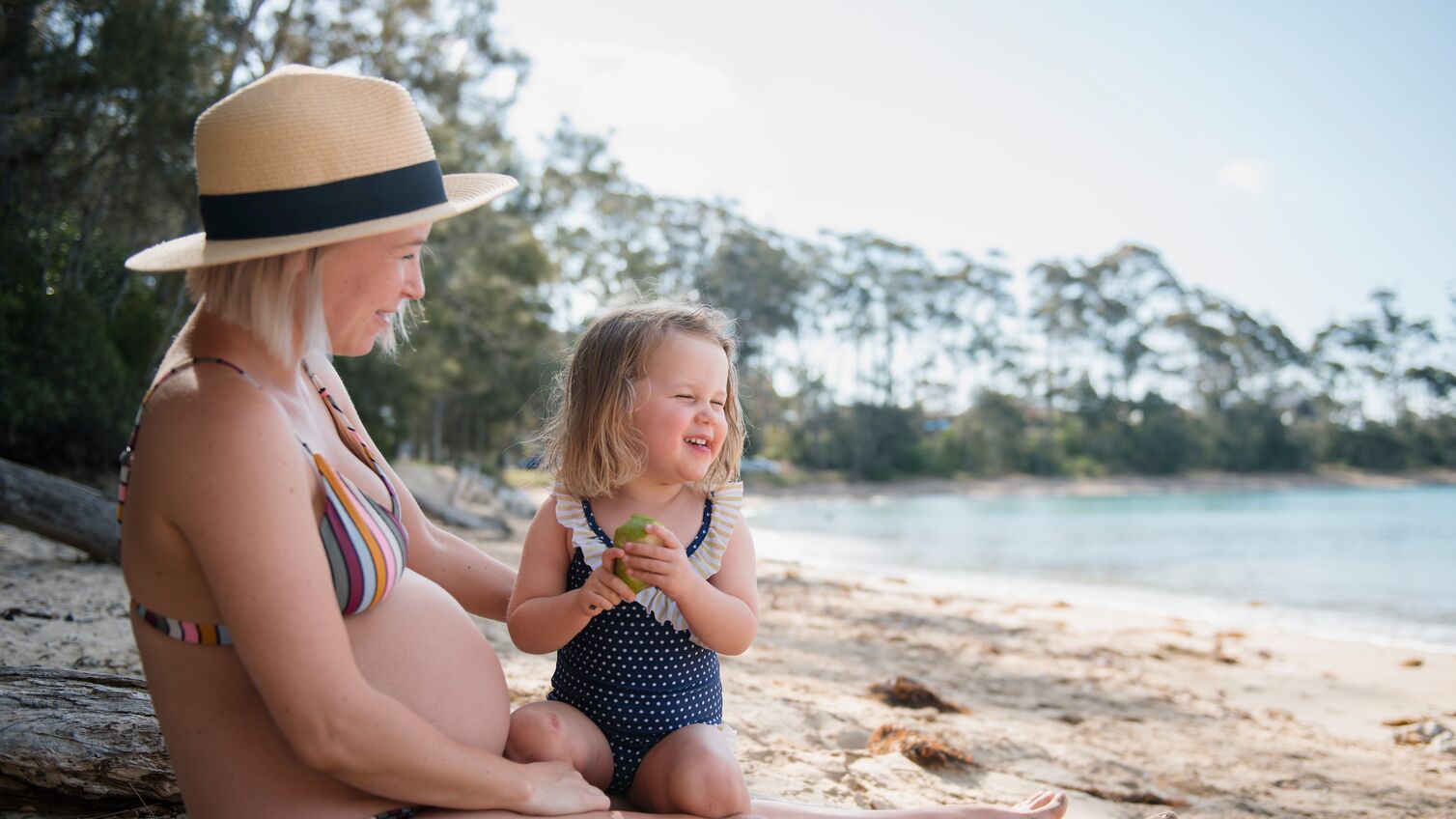 girl with pregnant mom sitting on sand at beach