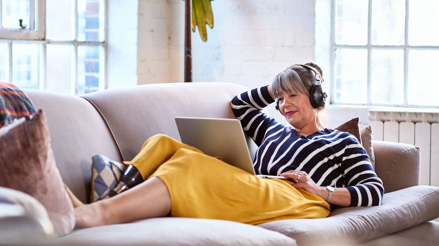 Woman in her 60s with prosthetic leg on sofa using laptop, relaxation, lifestyles, retirement