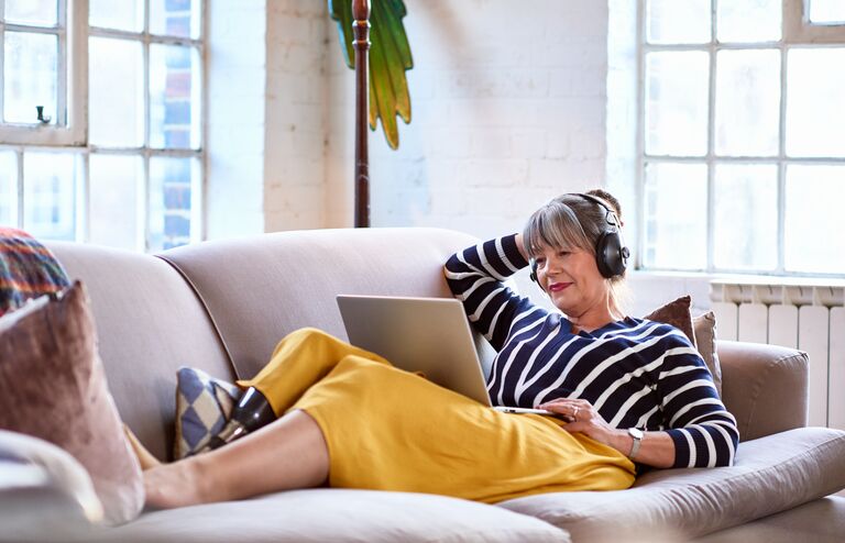 Woman in her 60s with prosthetic leg on sofa using laptop, relaxation, lifestyles, retirement