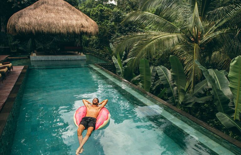 Shot of young man relaxing in resort swimming pool. Male on inflatable ring in pool.