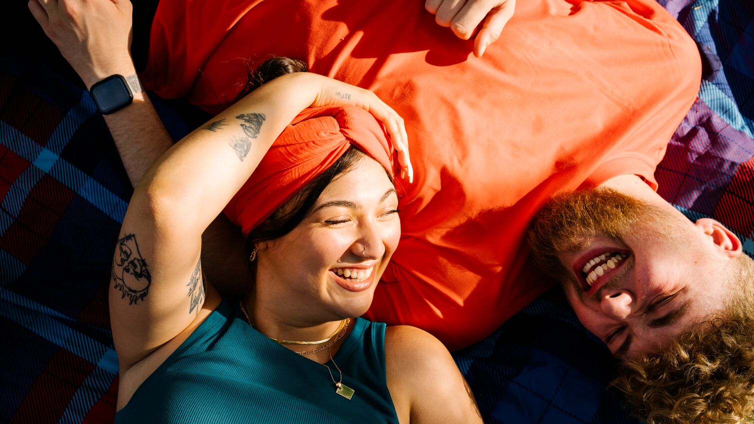 Top view shot of two young people generation z lying on a picnic blanket while the sun is shining in there faces and laughing at each other