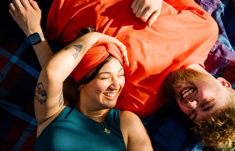 Top view shot of two young people generation z lying on a picnic blanket while the sun is shining in there faces and laughing at each other