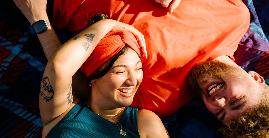Top view shot of two young people generation z lying on a picnic blanket while the sun is shining in there faces and laughing at each other