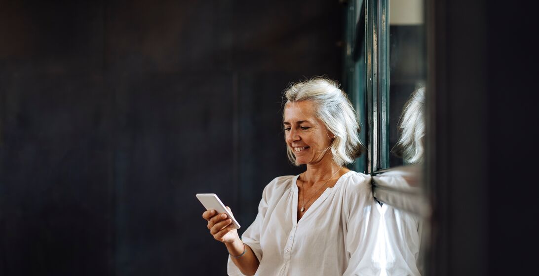 Smiling casual mature businesswoman using smartphone at the window in loft office