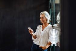 Smiling casual mature businesswoman using smartphone at the window in loft office