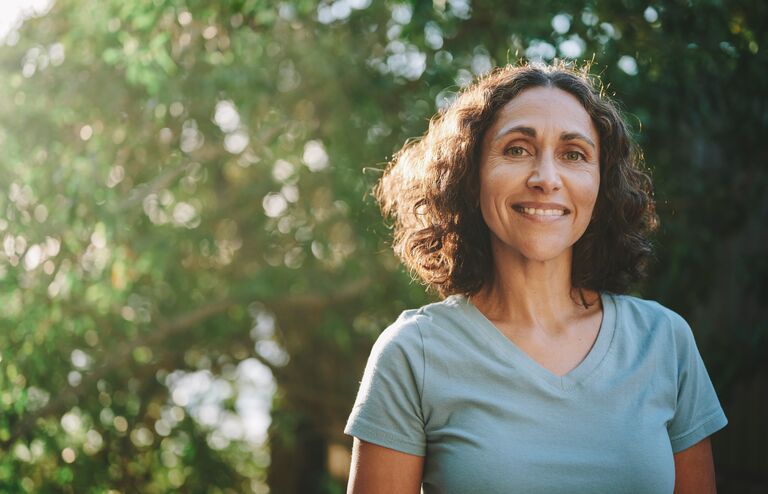 Portrait of a mature woman in sportswear smiling outside in a park on sunny day in summer