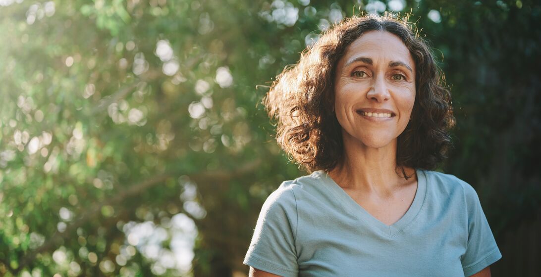 Portrait of a mature woman in sportswear smiling outside in a park on sunny day in summer