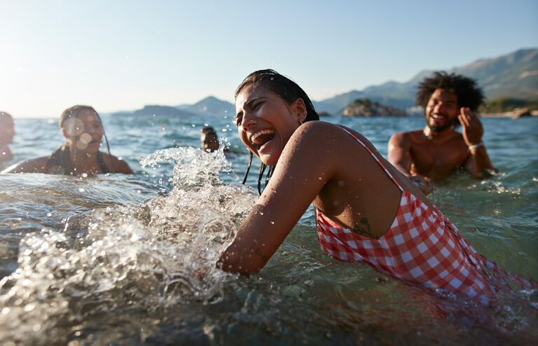 Cheerful young woman splashing water while enjoying swim with friends in sea on sunny day