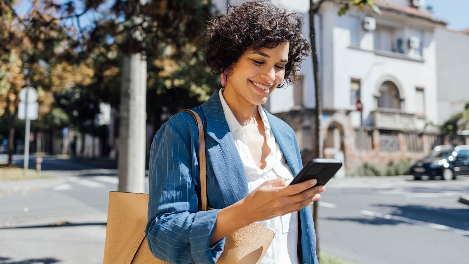 A mixed-race businesswoman reading something funny on her mobile phone on the street while going back home from work.