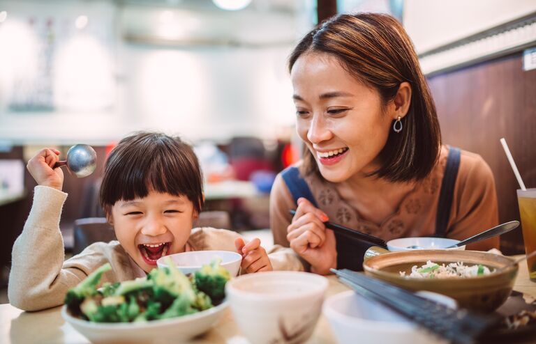 Pretty young mom enjoying meal with her lovely little daughter in the restaurant joyfully.