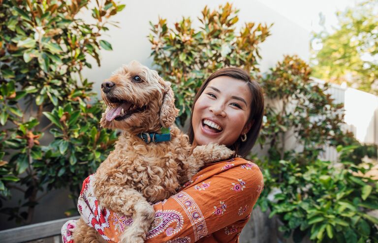 A shot of a young, Asian woman smiling at the camera with her dog.