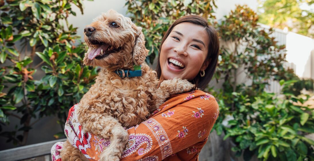 A shot of a young, Asian woman smiling at the camera with her dog.