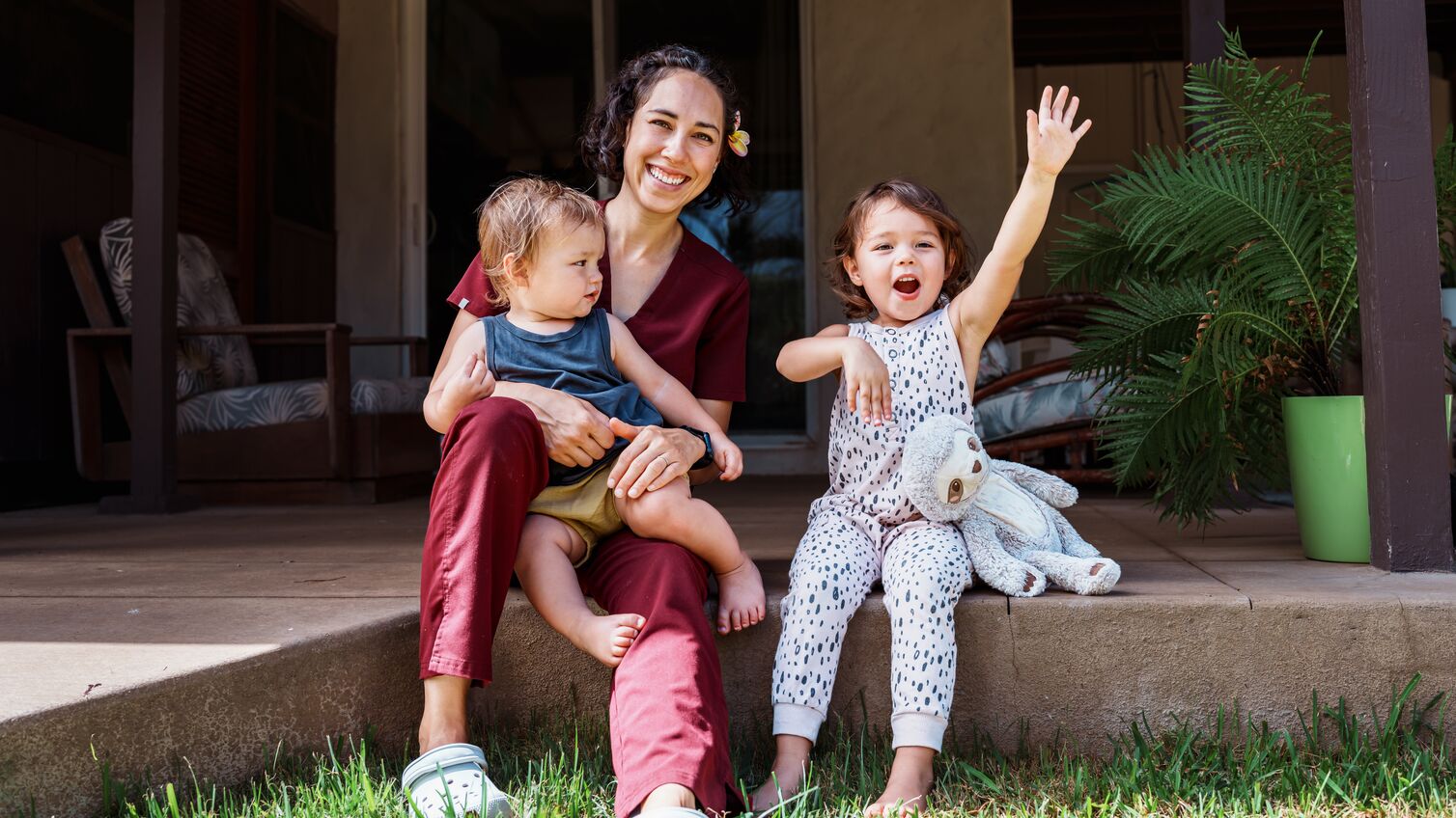 A female nurse of Hawaiian and Chinese descent sits outside on the back patio of her home and playfully interacts with her cheerful and cute Eurasian son and daughter after returning home from work.