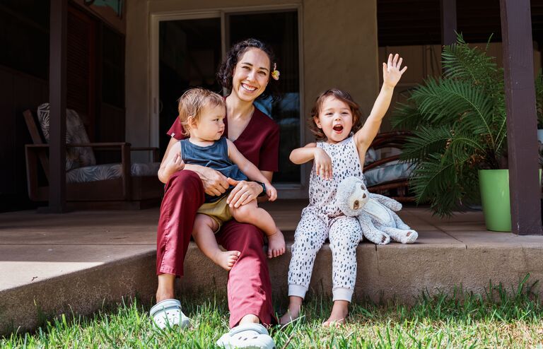 A female nurse of Hawaiian and Chinese descent sits outside on the back patio of her home and playfully interacts with her cheerful and cute Eurasian son and daughter after returning home from work.