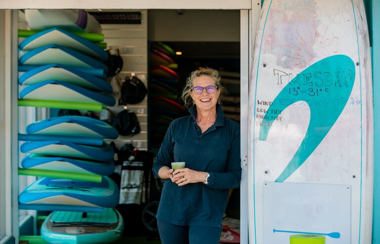 A shot of a mature woman stood at the door of her surf shop in Perth, Australia.