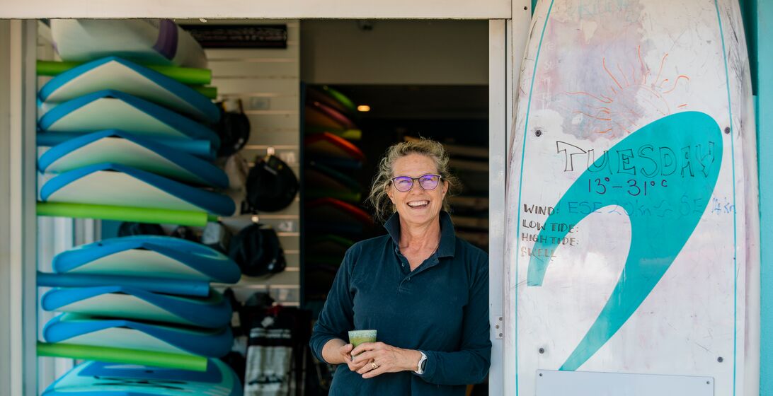 A shot of a mature woman stood at the door of her surf shop in Perth, Australia.