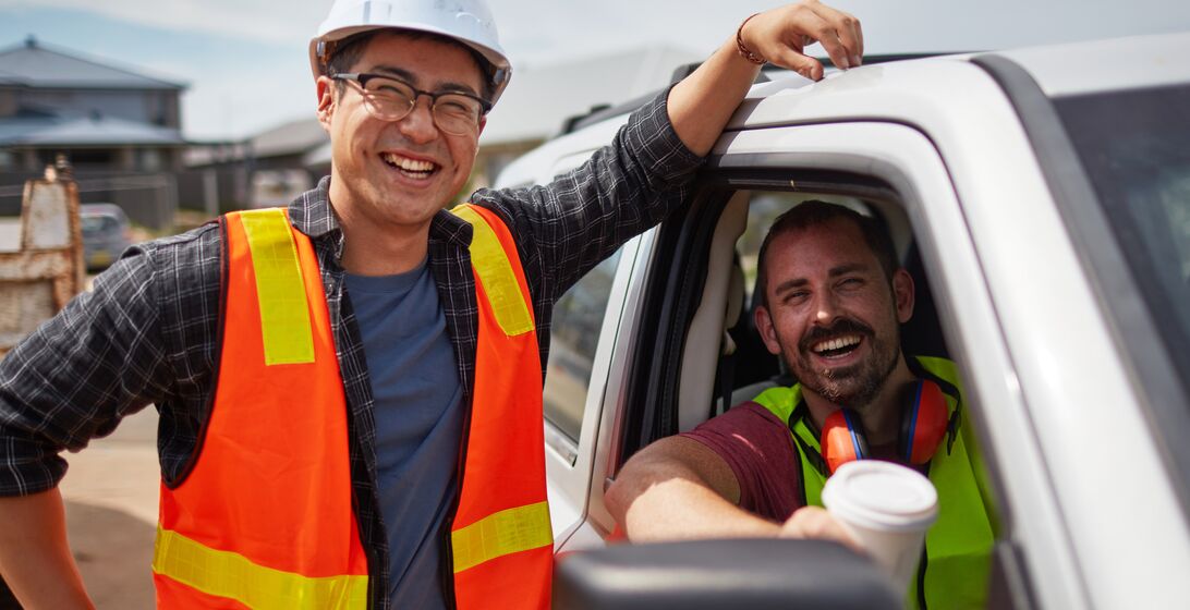 Portrait of worker smiling by colleague sitting in car. Male professionals are in reflective clothing. They are at construction site.