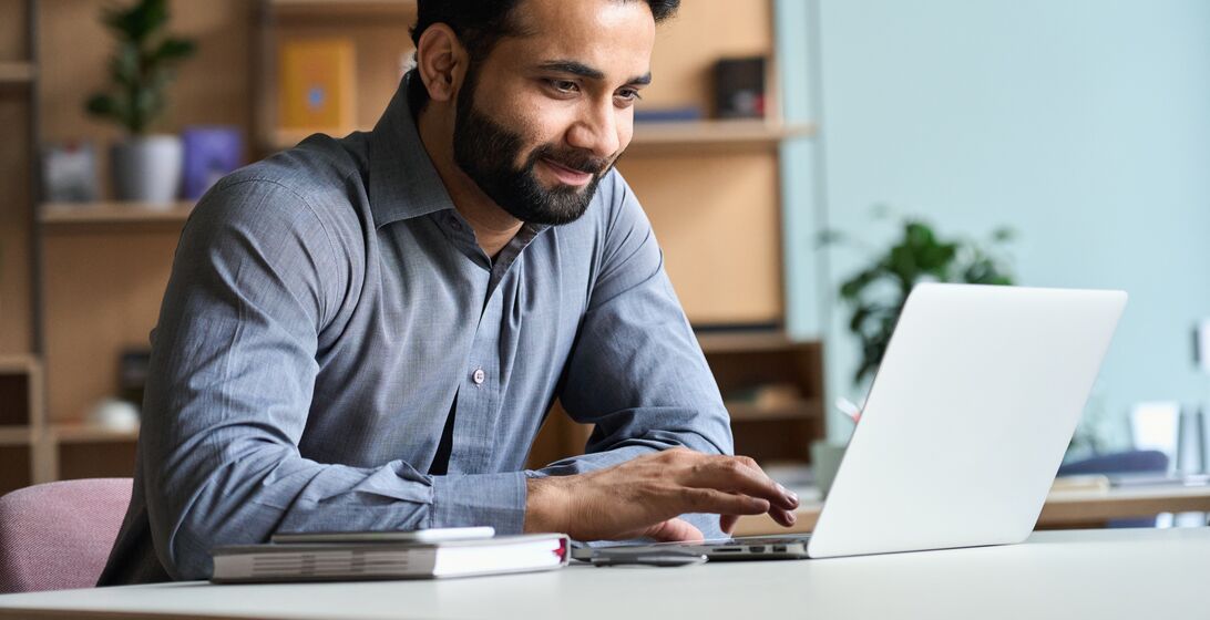 Smiling indian business man working on laptop at home office. Young indian student or remote teacher using computer remote studying, virtual training, watching online education webinar at home office.